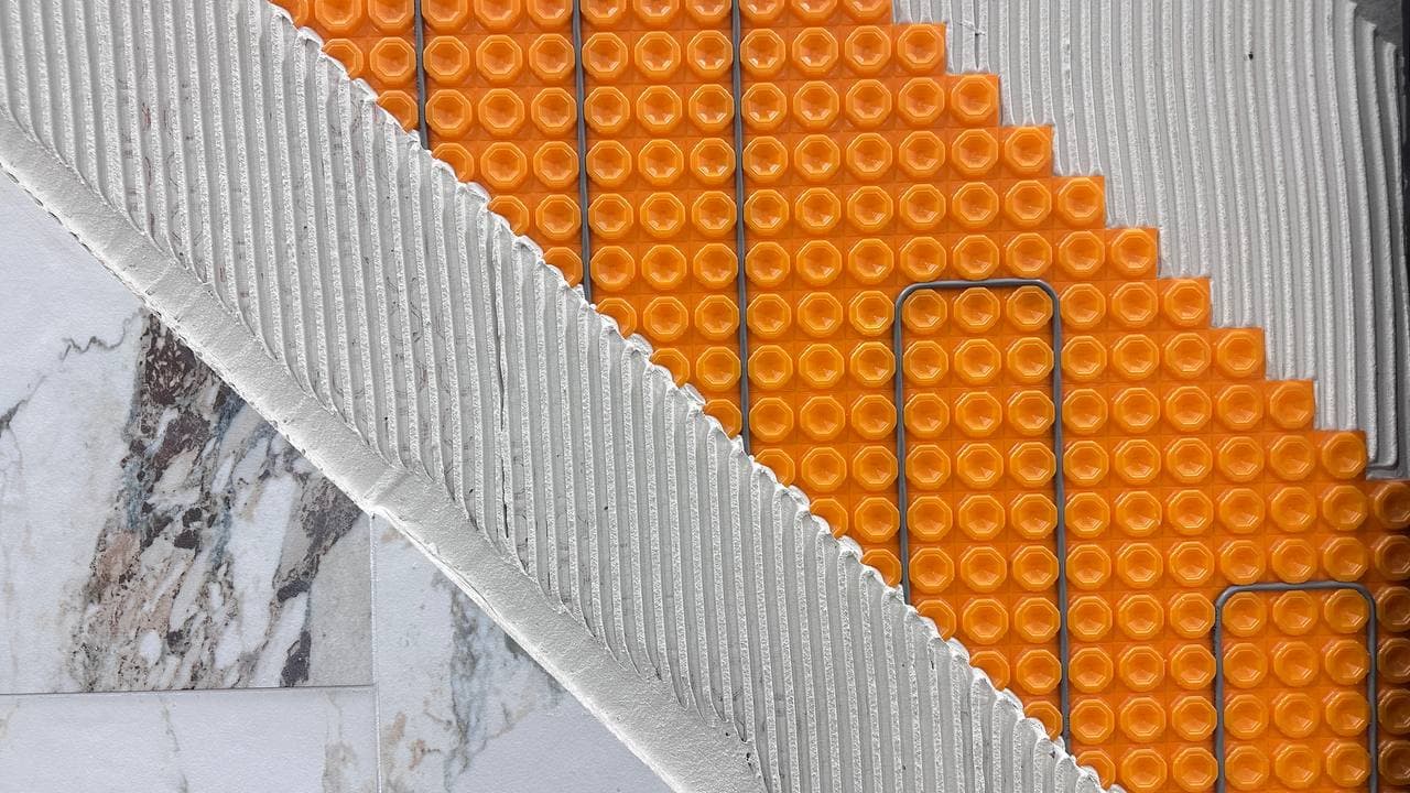 Heated floor installation with orange heating mats under marble tile in Denver bathroom