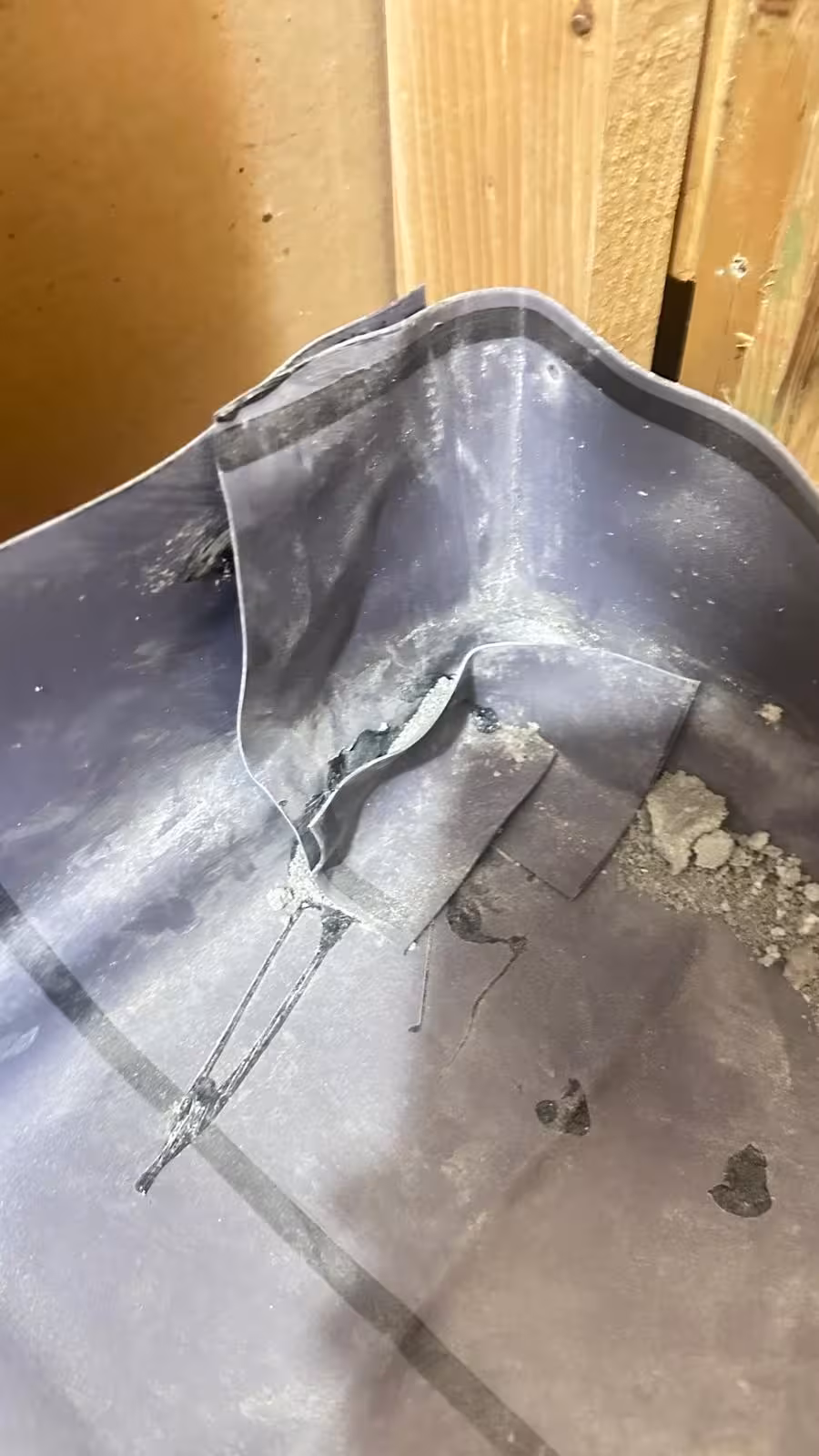 Cut shower pan liner corner in Denver area inspection showing torn waterproofing