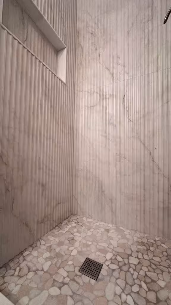 Before photo of outdated shower with beige tile and black accent stripe