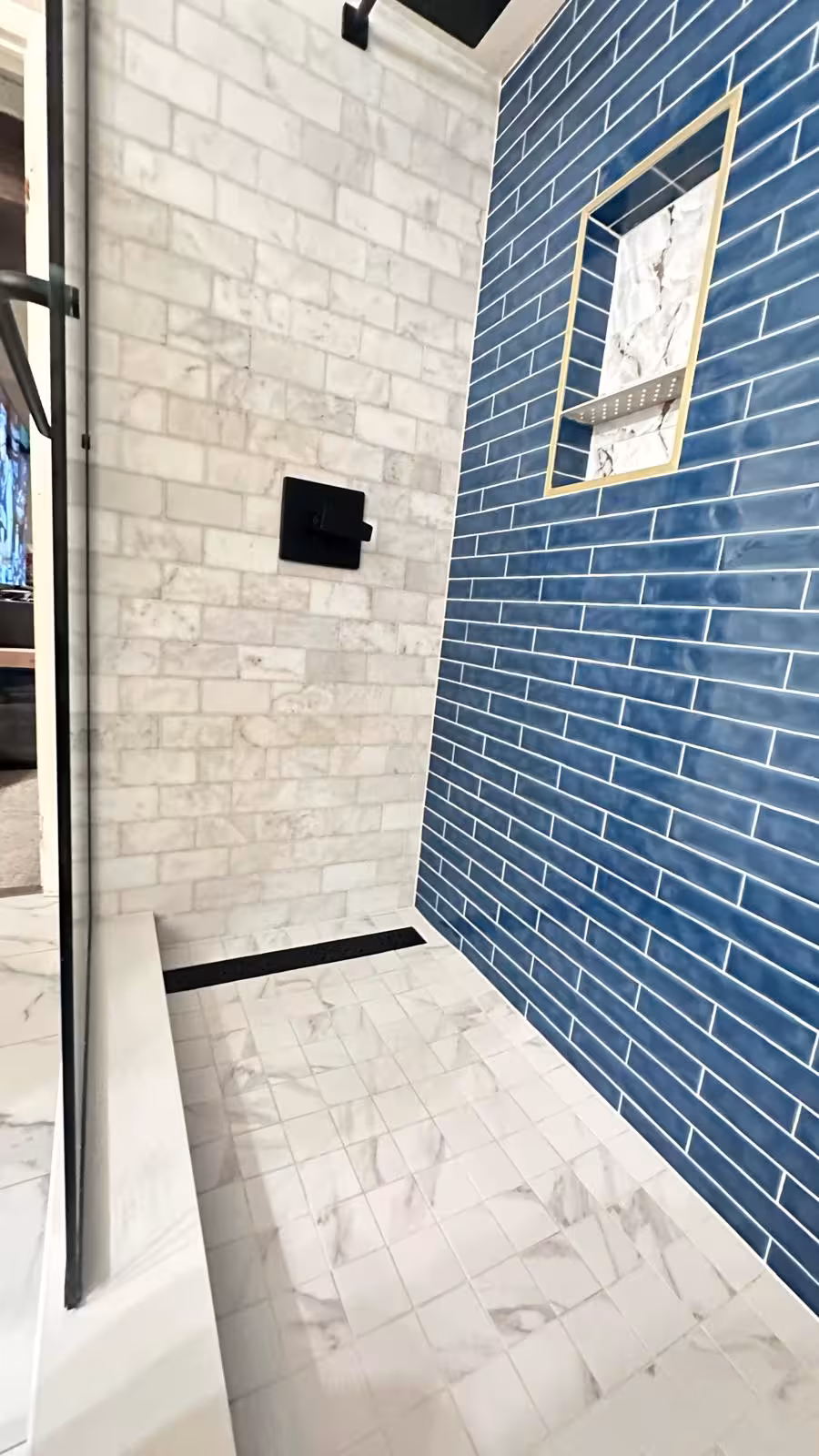 Interior view of custom basement shower with blue subway tile accent wall and marble surround