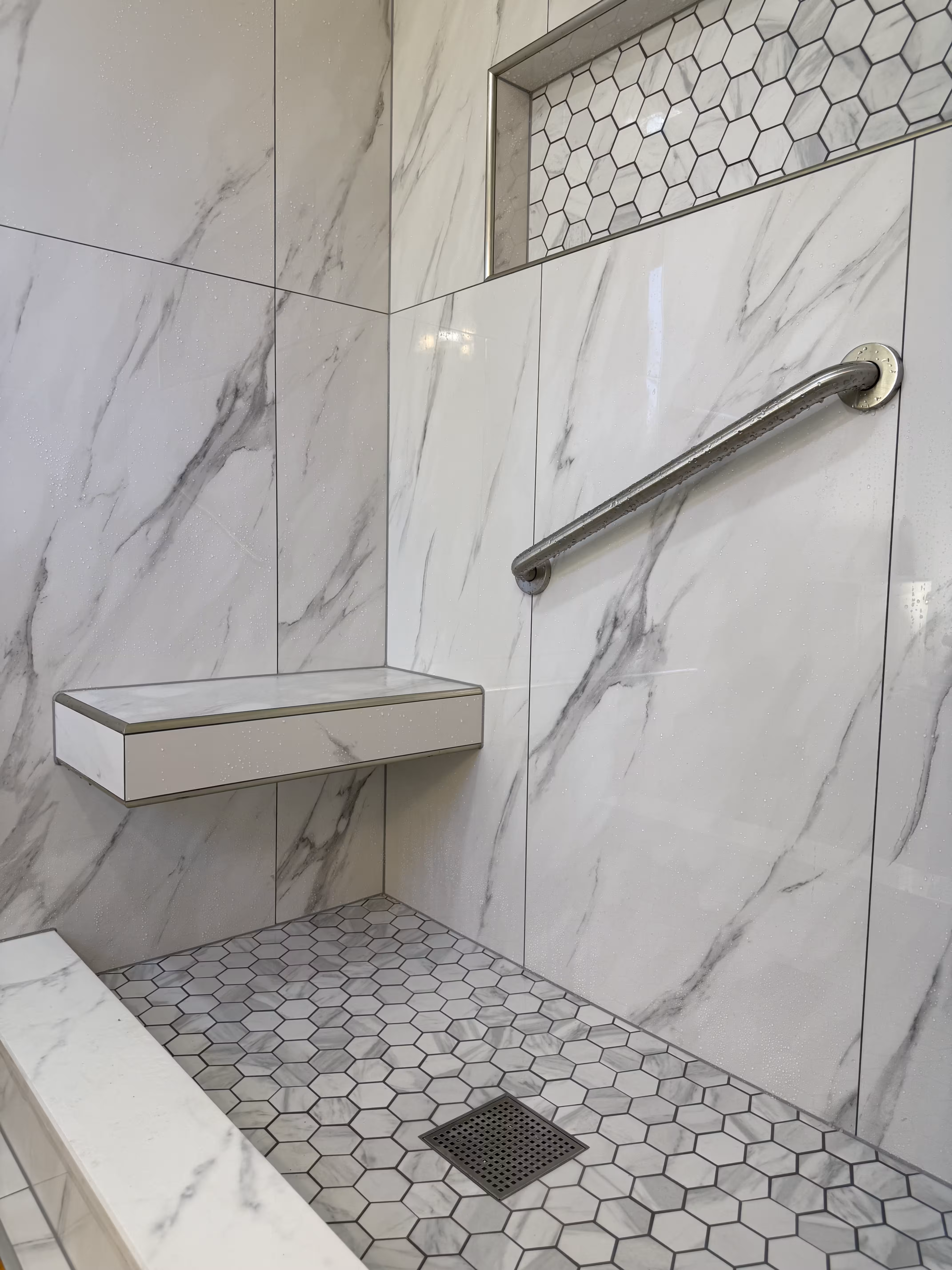 Finished shower with floating bench, large niche, hexagon floor tile and grab bar in Highlands Ranch