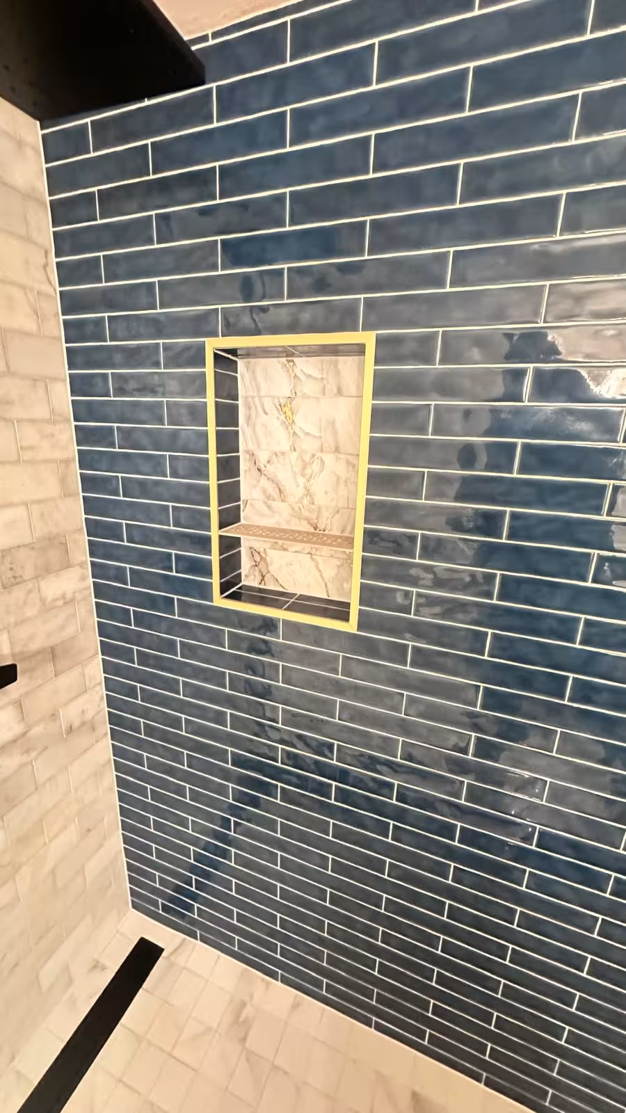 Built-in shower niche with Schluter gold trim and blue subway tile backsplash detail