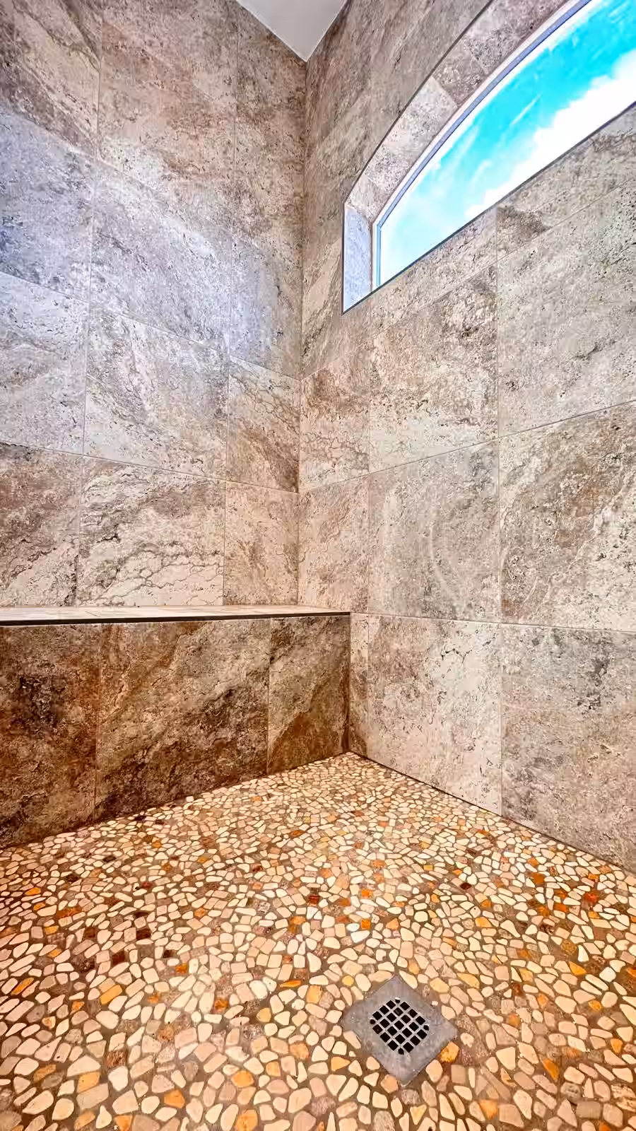 Finished luxury shower with pebble floor and natural stone tile walls