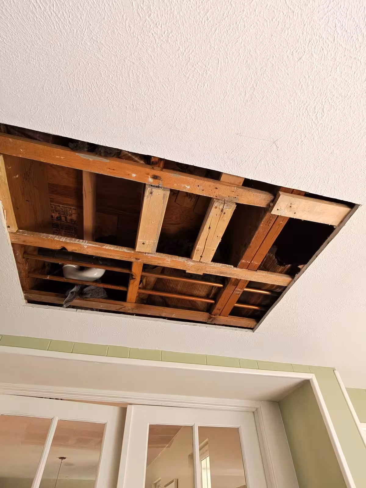 Large ceiling opening showing floor joists during shower pan inspection Denver
