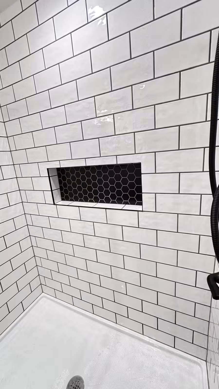 Subway tile shower niche with black hexagonal mosaic tile detail