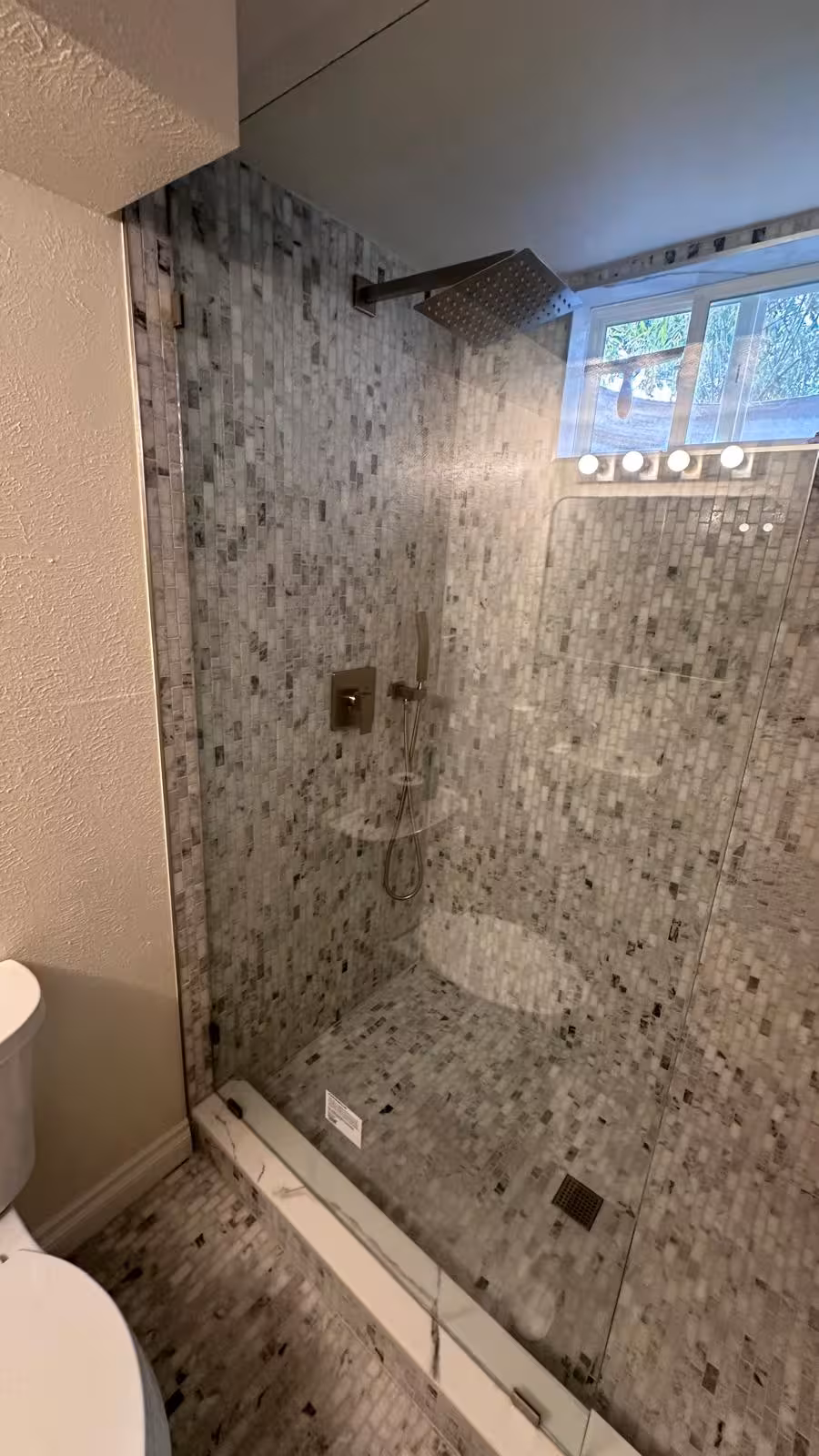 Frameless glass shower door with marble mosaic wall Littleton basement